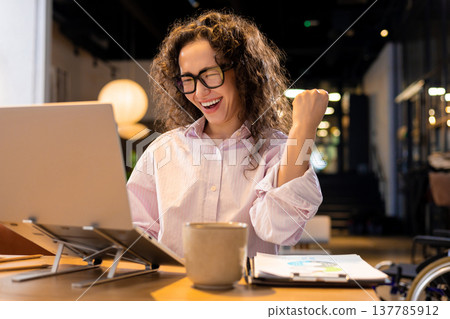 Happy woman winning with laptop raising hand posing in coworking office Happy woman winning with laptop raising hand posing in coworking office 137785912