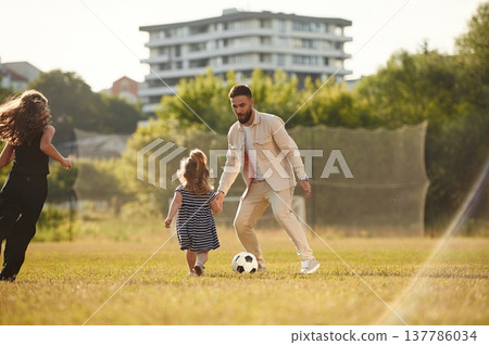 Man with his two daughters, playing on the field with soccer ball Man with his two daughters, playing on the field with soccer ball 137786034