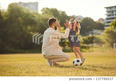 Giving high five, teamwork. Father with his little daughter are on the field Giving high five, teamwork. Father with his little daughter are on the field 137786037