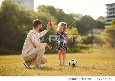 Giving high five, teamwork. Father with his little daughter are on the field Giving high five, teamwork. Father with his little daughter are on the field 137786039