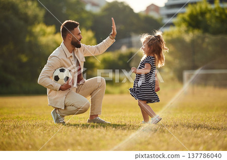 Giving high five, teamwork. Father with his little daughter are on the field Giving high five, teamwork. Father with his little daughter are on the field 137786040