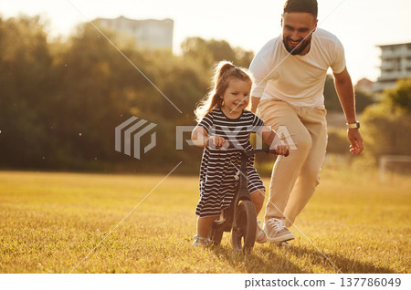 Riding the bicycle. Father with his little daughter are on the field 137786049