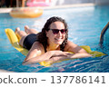 Happy woman relaxing on a yellow inflatable mattress in a sunny swimming pool 137786141
