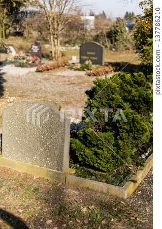 In a cemetery, several gravestones are visible with fresh flowers and decorations. The scene captures a moment of remembrance in broad daylight In a cemetery, several gravestones are visible with fresh flowers and decorations. The scene captures a moment of remembrance in broad daylight 137786210