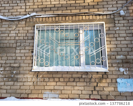 Brick facade with a window with a wrought-iron lattice on a sunny winter day Brick facade with a window with a wrought-iron lattice on a sunny winter day 137786218