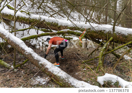 A male runner maneuvers through a snowy, obstacle-filled forest 137786378