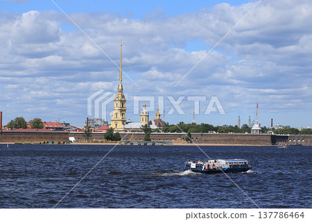 Russia, Petersburg, June 29, 2019. Spit of Vasilyevsky Island. The photo shows the Peter and Paul Fortress on the bank of the Neva against the sky and a pleasure boat with tourists admiring 137786464