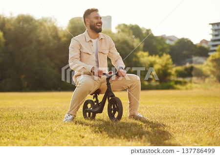 Adult man is on the kid's bicycle on the field 137786499