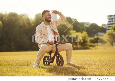 Adult man is on the kid's bicycle on the field 137786500