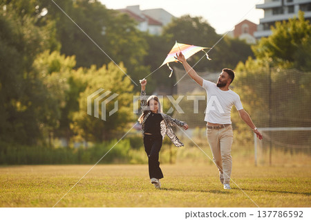 Front view, running with kite. Father with his little daughter are on the field Front view, running with kite. Father with his little daughter are on the field 137786592