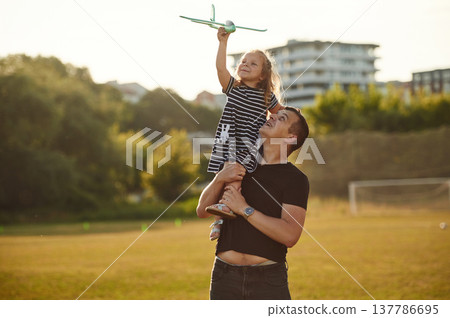 Looking up, holding toy plane, flying. Father with his little daughter are on the field 137786695