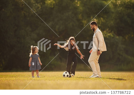 Man with his two daughters, playing on the field with soccer ball Man with his two daughters, playing on the field with soccer ball 137786722