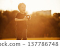 Small cute soccer ball in hands. Boy is having fun on the field at daytime 137786748