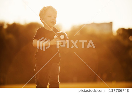 Small cute soccer ball in hands. Boy is having fun on the field at daytime Small cute soccer ball in hands. Boy is having fun on the field at daytime 137786748
