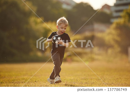 Small cute soccer ball in hands. Boy is having fun on the field at daytime Small cute soccer ball in hands. Boy is having fun on the field at daytime 137786749