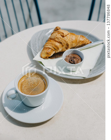 Cup of black coffee and a croissant on a table in a street cafe. Cup of black coffee and a croissant on a table in a street cafe. 137786848