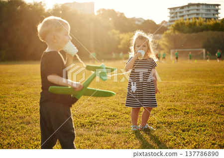 Conversation by using tin can telephone. Two kids are having fun on the summer field Conversation by using tin can telephone. Two kids are having fun on the summer field 137786890