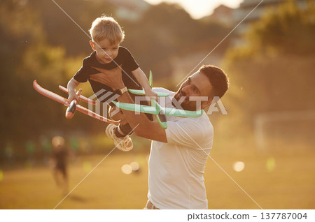 Come fly with me, holding kid in hands, toy plane. Happy father with son on the field Come fly with me, holding kid in hands, toy plane. Happy father with son on the field 137787004