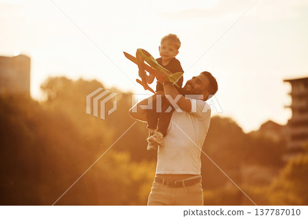 Against the white sky, with toy plane, flying. Happy father with son on the field Against the white sky, with toy plane, flying. Happy father with son on the field 137787010