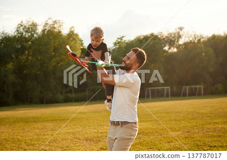 Cheerful, with toy plane, playing. Happy father with son on the field 137787017