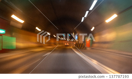 Motion blur of a vehicle driving through a tunnel with illuminated lights and colorful walls, showcasing the dynamic experience of urban transportation 137787193