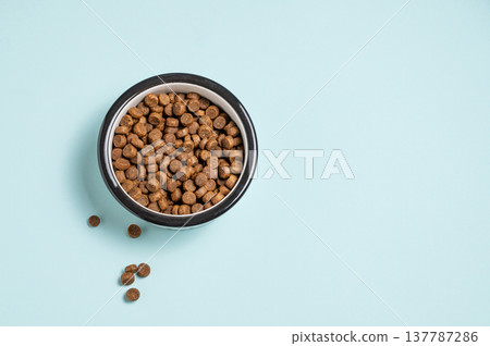 A bowl of dry dog food on a isolated blue background. A bowl of dry dog food on a isolated blue background. 137787286