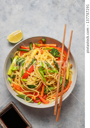 Stir fry wok noodles with vegetables in a plate on a light background with chopsticks, soy sauce Stir fry wok noodles with vegetables in a plate on a light background with chopsticks, soy sauce 137787291