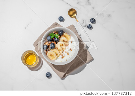 Greek yogurt with granola, blueberry and banana in a bowl on a marble background with honey 137787312