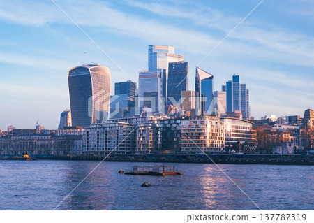Morning light bathes the modern skyline of London as the Thames river gently flows by. Skyscrapers rise above the city, creating a stunning urban landscape. Morning light bathes the modern skyline of London as the Thames river gently flows by. Skyscrapers rise above the city, creating a stunning urban landscape. 137787319