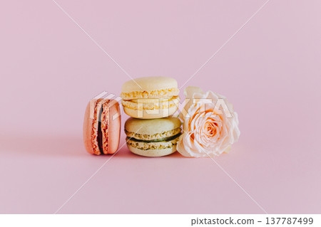 Tasty french macarons with tender rose flowers on a pink pastel background. Tasty french macarons with tender rose flowers on a pink pastel background. 137787499