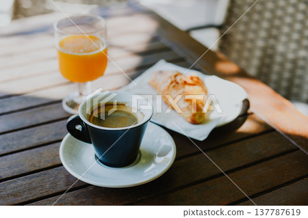 Cup of black coffee, a croissant and glass of fresh orange juice on a table in a street cafe. Cup of black coffee, a croissant and glass of fresh orange juice on a table in a street cafe. 137787619