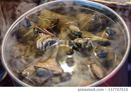 Steaming pot of leaf-wrapped dumplings cooking under lid Steaming pot of leaf-wrapped dumplings cooking under lid 137787818