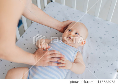 Mother sitting beside the crib gently stroking her baby lying in a cozy bed at home. Warm intimate moment filled with love, trust and calm. Motherhood, infant comfort and emotional bonding concept 137788078