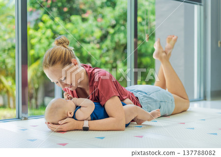 Mother and baby lying on a soft play mat at home, playing, talking and sharing a joyful moment together. Authentic family lifestyle, early childhood development and emotional bonding. Parenting and Mother and baby lying on a soft play mat at home, playing, talking and sharing a joyful moment together. Authentic family lifestyle, early childhood development and emotional bonding. Parenting and 137788082
