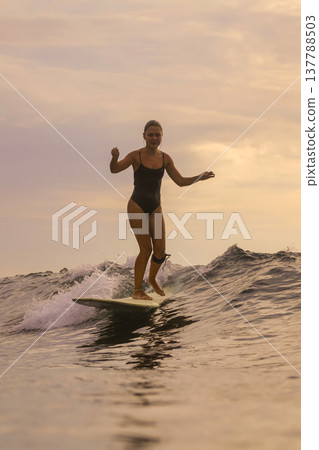 Relaxed Female Rider Gliding On Longboard At Sunset Over Gentle Waters Relaxed Female Rider Gliding On Longboard At Sunset Over Gentle Waters 137788503