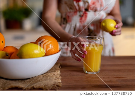 Woman holding lemon over glass, floral dress and wooden surface, bowl of citrus in foreground, fresh juice preparation, vitaminC wellness moment, influencerstyle natural light Woman holding lemon over glass, floral dress and wooden surface, bowl of citrus in foreground, fresh juice preparation, vitaminC wellness moment, influencerstyle natural light 137788750