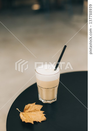 Glass of tasty latte and yellow leaf on a table in a street cafe. 137788939