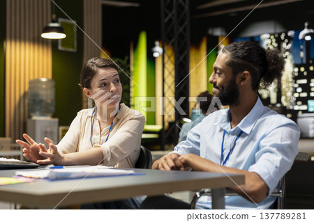 Discussing, sharing project ideas and cheerful employees in relaxed coworking space. Collaborating, pleasant conversation and smiling coworkers at office desk finishing work tasks 137789281