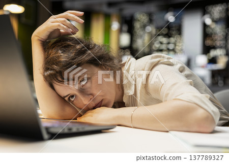 Businesswoman struggling to stay awake after an intense workload, lounges across desk at midnight. Fatigue, mental haze and workplace challenges have left her drained and restless. 137789327