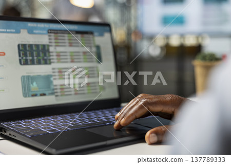 Financial analyst at desk evaluating investment opportunities and company stock performance on laptop. African American office employee studying online market projections and data on device. Financial analyst at desk evaluating investment opportunities and company stock performance on laptop. African American office employee studying online market projections and data on device. 137789333