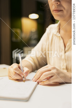 Close up of female staff transcribing important key points for presentation late at night, doing overtime to finish her pitch Planning and scheduling tasks, notetaking and handwriting. Close up of female staff transcribing important key points for presentation late at night, doing overtime to finish her pitch Planning and scheduling tasks, notetaking and handwriting. 137789334