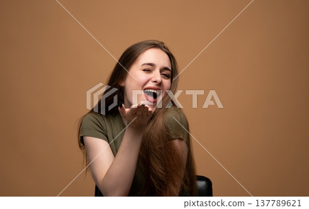 Young woman winking, smiling, and blowing a kiss with a happy, flirty, and playful expression on a brown background 137789621