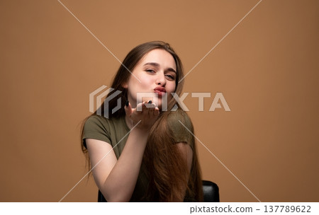 Young woman blowing an air kiss with pursed lips, embodying femininity, charm, and emotional expression 137789622