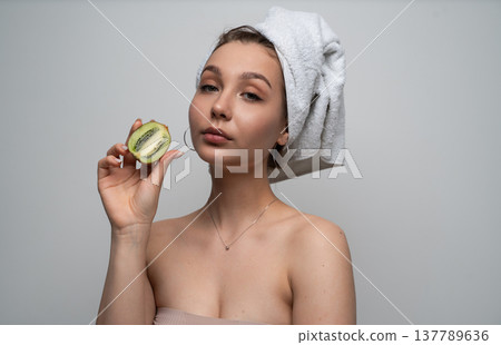 Young woman with a towel wrapped around her hair, holding a fresh kiwi fruit half, representing natural skincare, organic beauty, health, glow, and wellness concepts Young woman with a towel wrapped around her hair, holding a fresh kiwi fruit half, representing natural skincare, organic beauty, health, glow, and wellness concepts 137789636