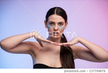 Young woman applying under eye patches on her face, embracing a beauty and self-care routine for skin hydration and rejuvenation with a gentle expression and neat ponytail Young woman applying under eye patches on her face, embracing a beauty and self-care routine for skin hydration and rejuvenation with a gentle expression and neat ponytail 137789678