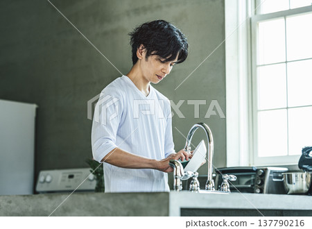一位年輕男子正在廚房洗碗。 一位年輕男子正在廚房洗碗。 137790216