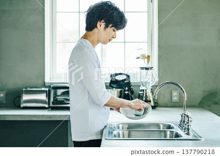 一位年輕男子正在廚房洗碗。 137790218