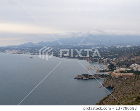 Seaside Landscape With Distant Mountains, Serene Coast With Urban Skyline And Shimmering Sea Seaside Landscape With Distant Mountains, Serene Coast With Urban Skyline And Shimmering Sea 137790588