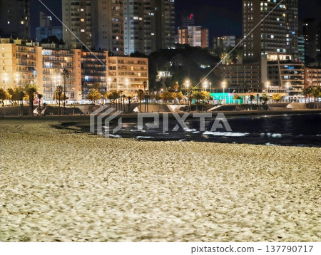Beach Lights Sparkle, Silvery Reflections Dance On Sand Beneath Distant Skyscrapers And Gentle Sea Movements Beach Lights Sparkle, Silvery Reflections Dance On Sand Beneath Distant Skyscrapers And Gentle Sea Movements 137790717