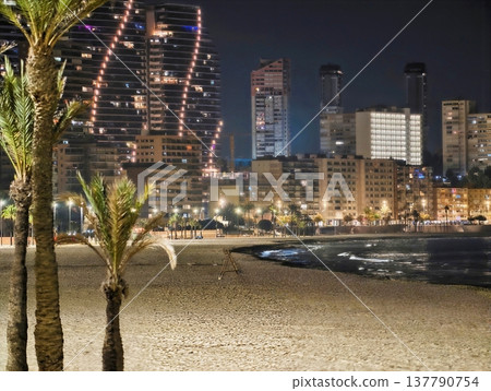 Tranquil Evening Seashore Featuring Shimmering Highrise Reflections And Softly Rippling Waves Across Wet Sands Tranquil Evening Seashore Featuring Shimmering Highrise Reflections And Softly Rippling Waves Across Wet Sands 137790754
